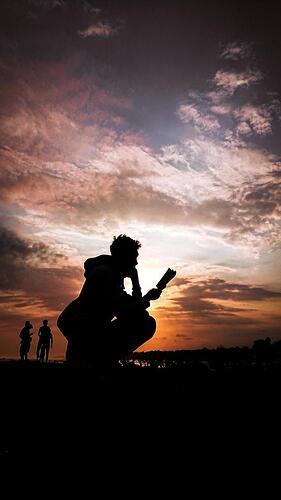 silhouette-of-a-man-reading-a-book-at-sunset-free-photo