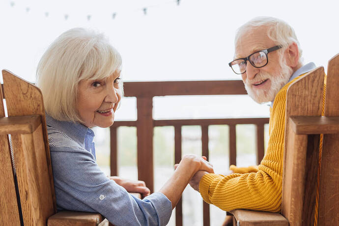 stock-photo-smiling-elderly-couple-looking-camera-holding-hands-while-sitting-armchairs